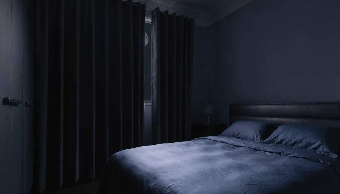 A dark bedroom with blackout curtains parted to reveal faint moonlight