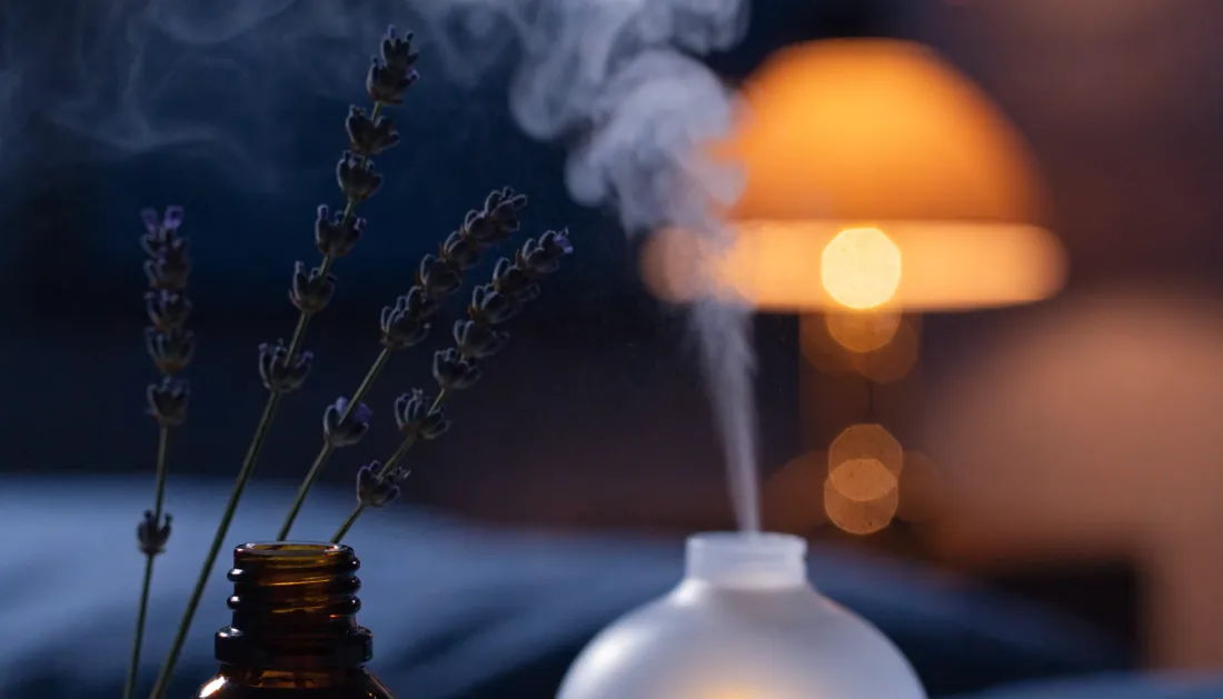 An amber essential oil bottle with lavender beside a softly misting diffuser