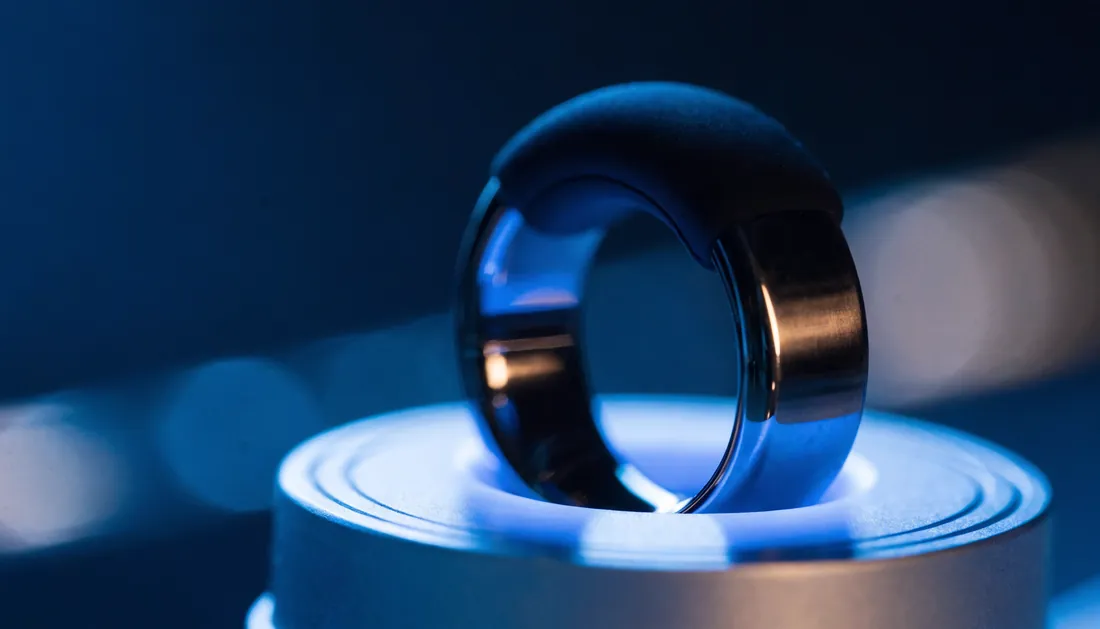 A smart sleep tracking ring resting on its charging dock with a blue glow